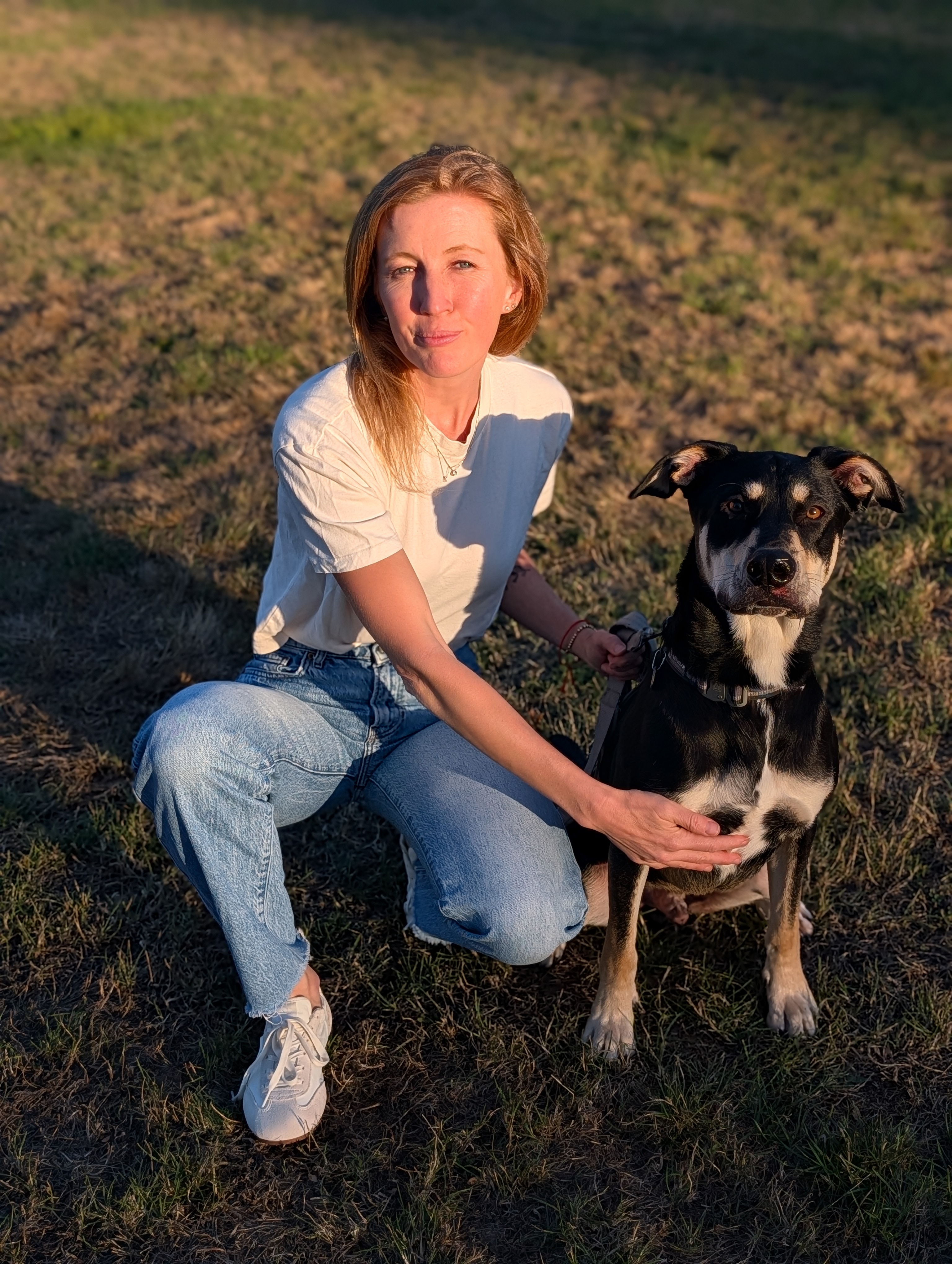 Kate Nelson sitting outdoors with a black and tan dog